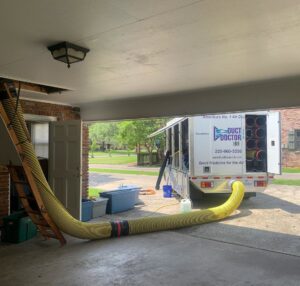 Residential air duct cleaning setup with a large yellow hose connecting the attic to a service truck from Duct Doctor of Baton Rouge, LA.