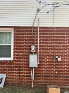 A residential electrical meter and service panel on the exterior brick wall of a house, serviced by Kaufman Electric in Greensboro, NC.