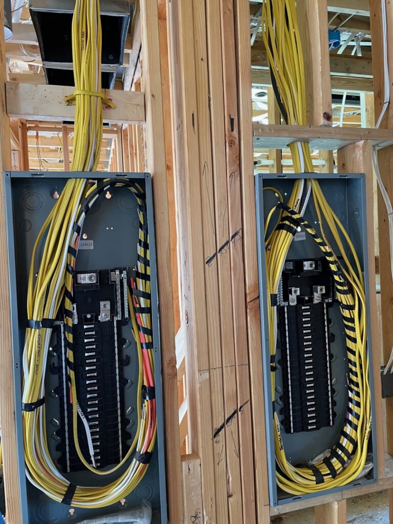 Electrical rough-in with two breaker panels and yellow wiring in a framed residential wall by Industrial Edge Electrical in Gilbert, AZ.