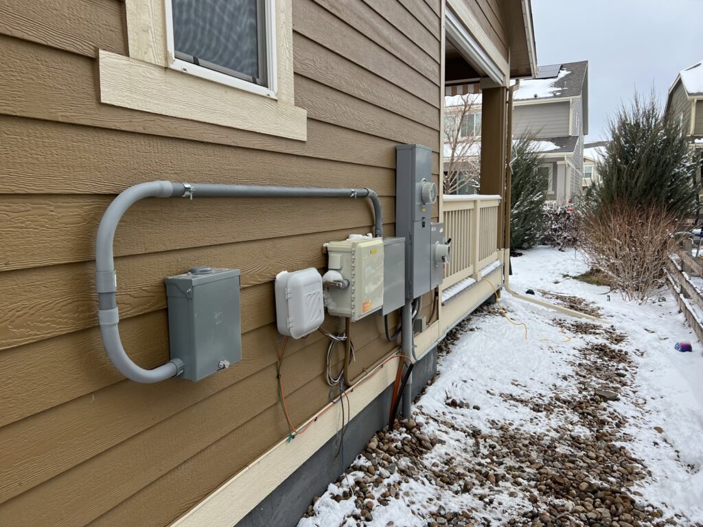 Exterior view of a residential electrical service installation with meters and conduits by P&E Electric in Denver, CO.