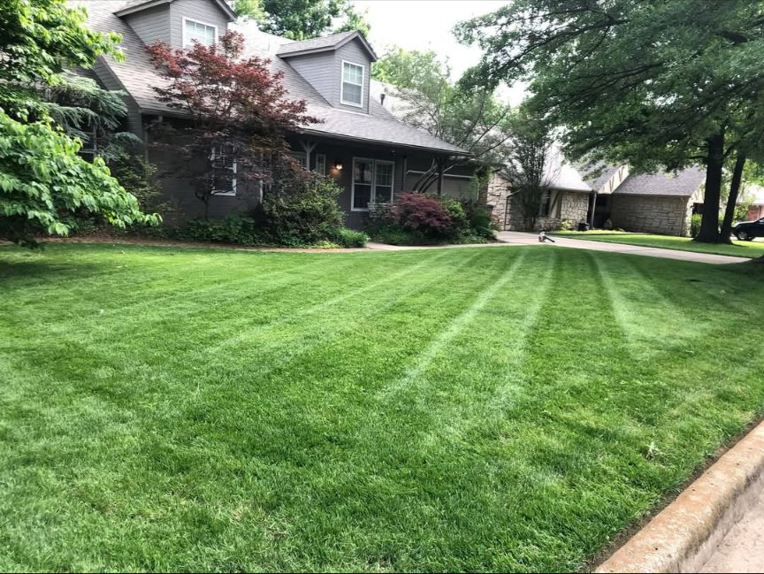 A residential front lawn showcasing perfectly mowed grass with distinct stripes, a testament to Lande Lawn Care in Broken Arrow, OK.