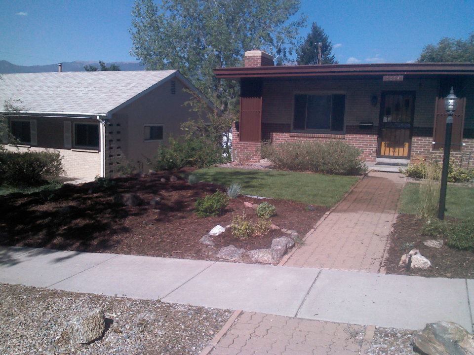 A completed residential front yard landscaping project with mulch beds and a green lawn by RMMLS in Colorado Springs, CO.