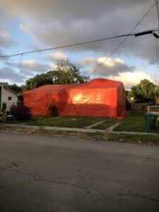 A residential house covered in a red tarp for pest control fumigation by Globe Pest Inc in Miami, FL, during evening light.
