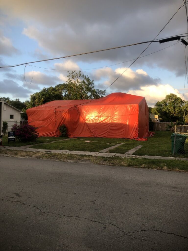 A residential house covered in a red tarp for pest control fumigation by Globe Pest Inc in Miami, FL, during evening light.
