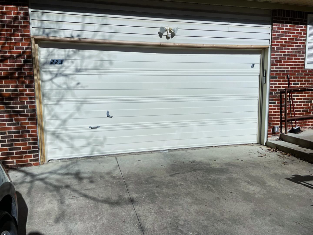 A white residential garage door on a brick house, ready for service from Horton & Hill Garage Door Specialists LLC in Sapulpa, OK.