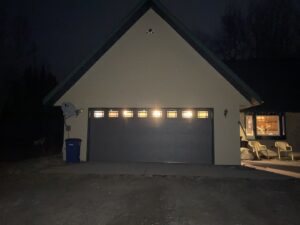 A residential grey garage door with windows illuminated at night by AJK Door Services in Duluth, MN.