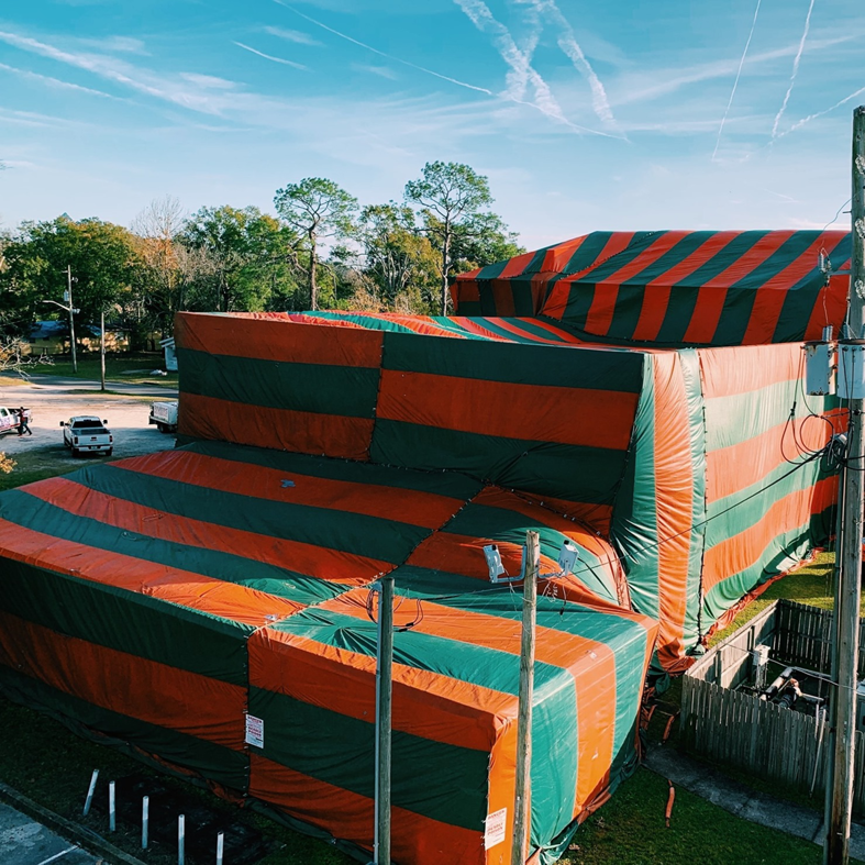 A residential house covered in a red and green fumigation tent by Rivers Pest Control Service, Inc. in Jacksonville, FL