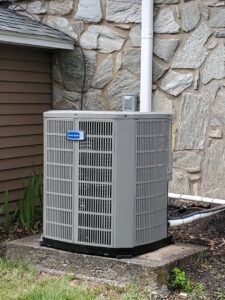 A residential outdoor HVAC condenser unit installed next to a stone wall by Capitol Heating and Air in Morgantown, PA.