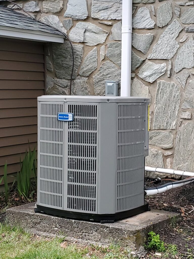 A residential outdoor HVAC condenser unit installed next to a stone wall by Capitol Heating and Air in Morgantown, PA.