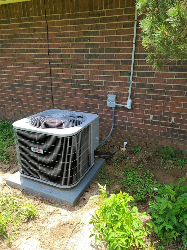A residential HVAC condenser unit installed outside a home with a brick wall by Fusion Heat and Air in Fort Smith, AR.