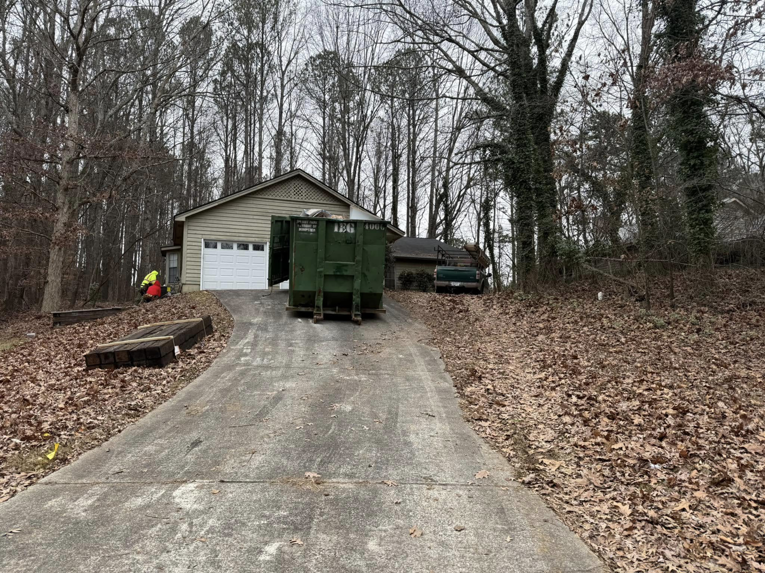 A large green dumpster in a residential driveway for junk removal services by Helping Hand HVAC & Maintenance in Atlanta, GA.