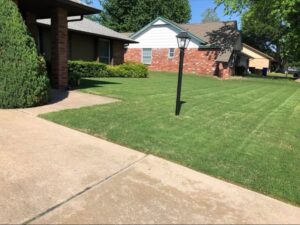 A residential front lawn freshly mowed with visible stripes, showcasing professional lawn care by Lande Lawn Care in Broken Arrow, OK.