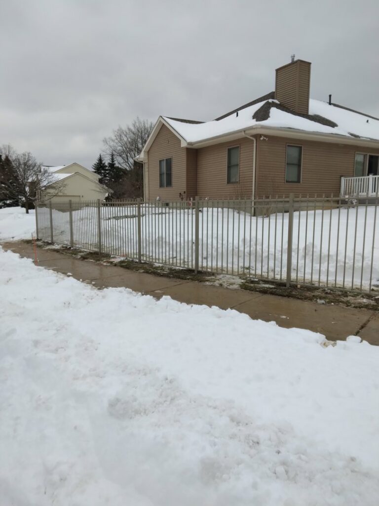 A new metal fence installed along a sidewalk in a snowy residential area by Sparta Fencing in Ely, UK.