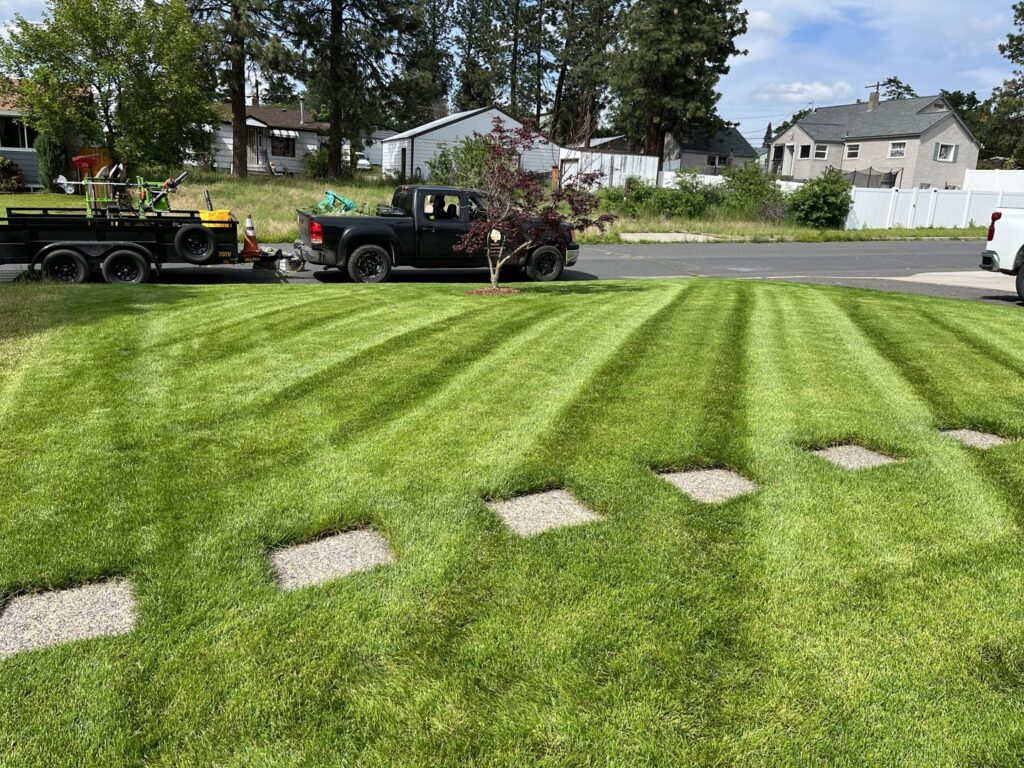A residential lawn with perfect mowing stripes and stepping stones, with lawn care equipment on a trailer in the background by McLain Lawn & Landscape in Spokane, WA.