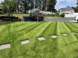 A residential lawn with perfect mowing stripes and stepping stones, with lawn care equipment on a trailer in the background by McLain Lawn & Landscape in Spokane, WA.
