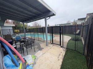 A residential swimming pool enclosed by a black mesh safety fence and gate from Golden State Baby Barrier in Sacramento, CA.