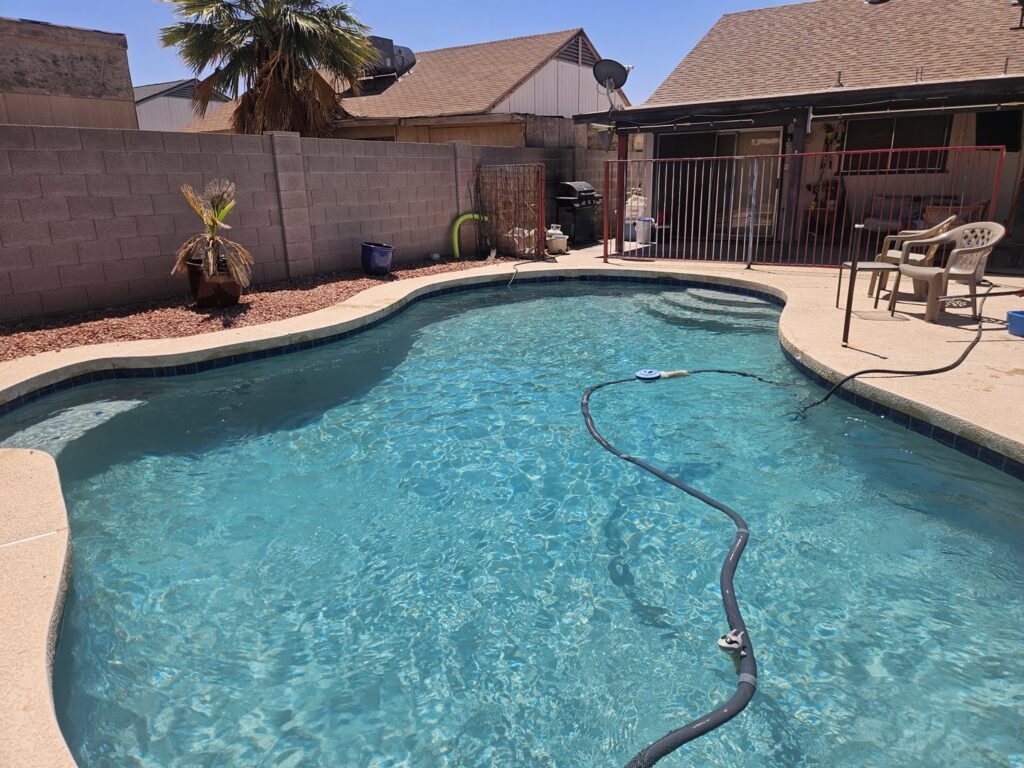 A residential swimming pool with an automatic pool cleaner hose in the water by Vanguard Pool Care in Phoenix, AZ