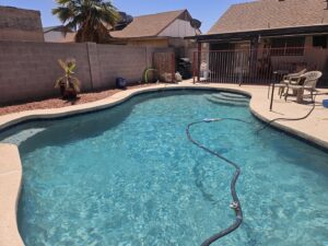 A residential swimming pool with an automatic pool cleaner hose in the water by Vanguard Pool Care in Phoenix, AZ