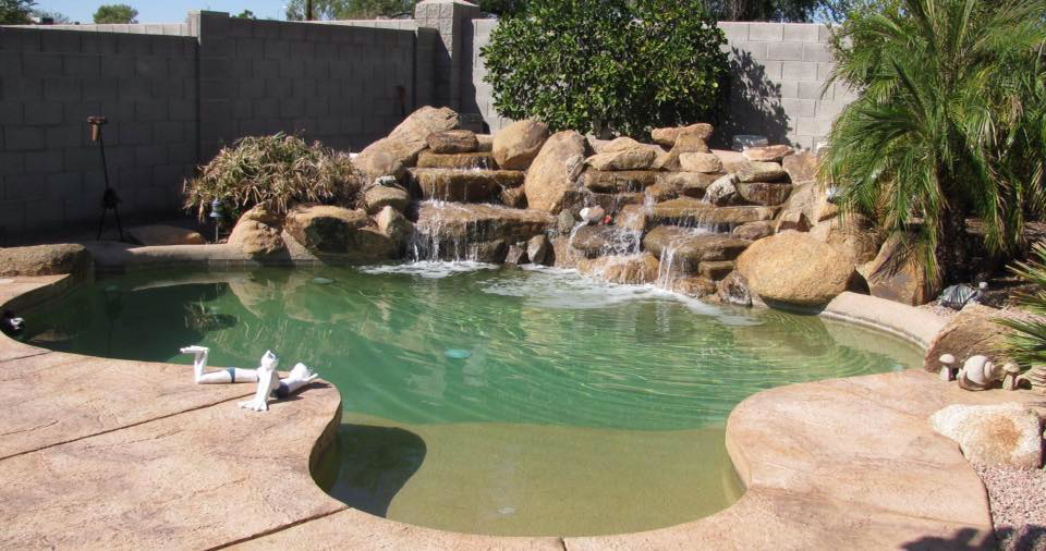 A residential pool with a rock waterfall and visible cleaning tools, indicating service by Serkland's Pool Service in Phoenix, AZ.