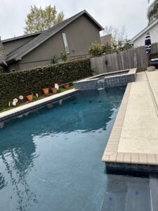 A residential swimming pool featuring a dark plaster finish and an attached spa, completed by I10 Pool Plastering LLC in Kenner, LA.