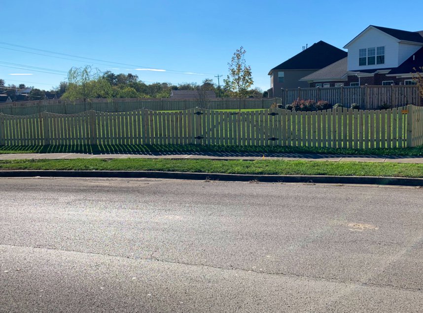 A long, attractive scalloped wooden privacy fence bordering a residential property, installed by Roark Fencing in Lexington, KY.