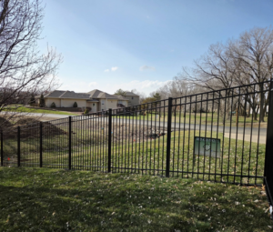 A black metal fence installed along a residential street, with a Green Acres Fence Co sign visible in Salina, KS.