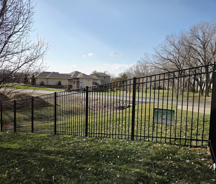 A black metal fence installed along a residential street, with a Green Acres Fence Co sign visible in Salina, KS.