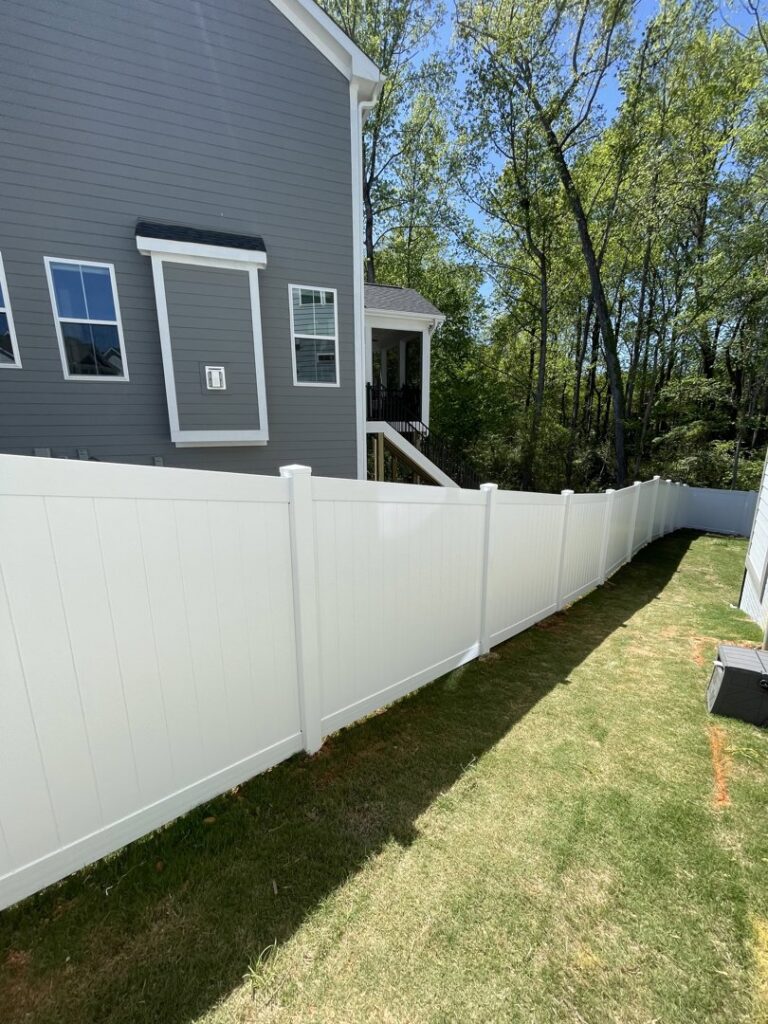 A long white vinyl privacy fence installed in a residential backyard with a house in the background by RDU Fence in Holly Springs, NC.