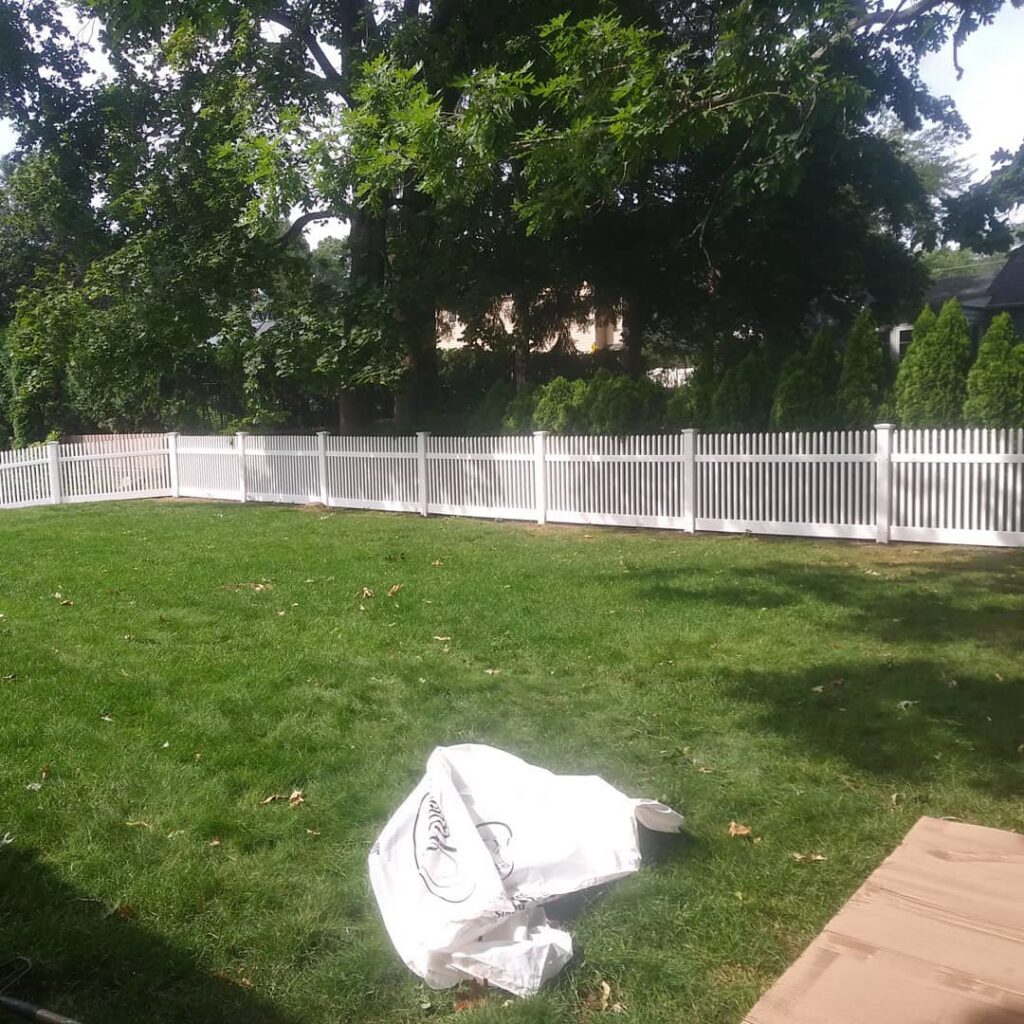 A classic white vinyl picket fence enclosing a residential backyard, installed by Reilly Fence Inc in Cranston, RI.