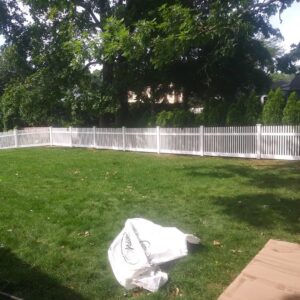 A classic white vinyl picket fence enclosing a residential backyard, installed by Reilly Fence Inc in Cranston, RI.