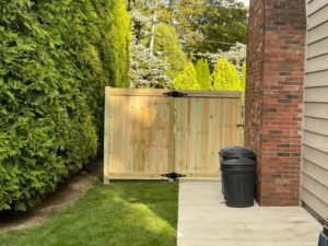 A residential wood gate installed between a brick wall and a hedge by STILL Fencing in Rochester, NY.