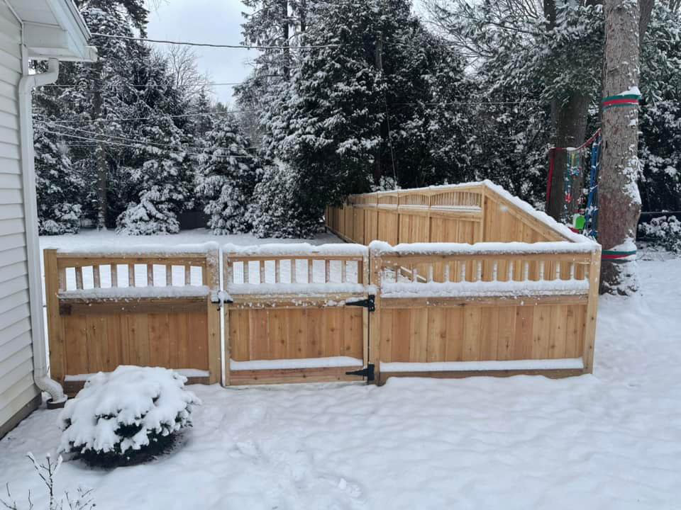 A residential wood privacy fence with a gate, covered in snow, installed by STILL Fencing in Rochester, NY.