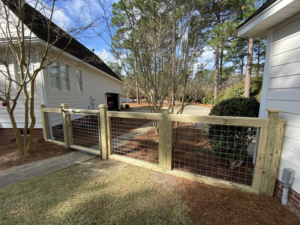 A residential wood and wire mesh fence with a gate next to a house by Renegade Fencing, LLC in Jacksonville, NC.