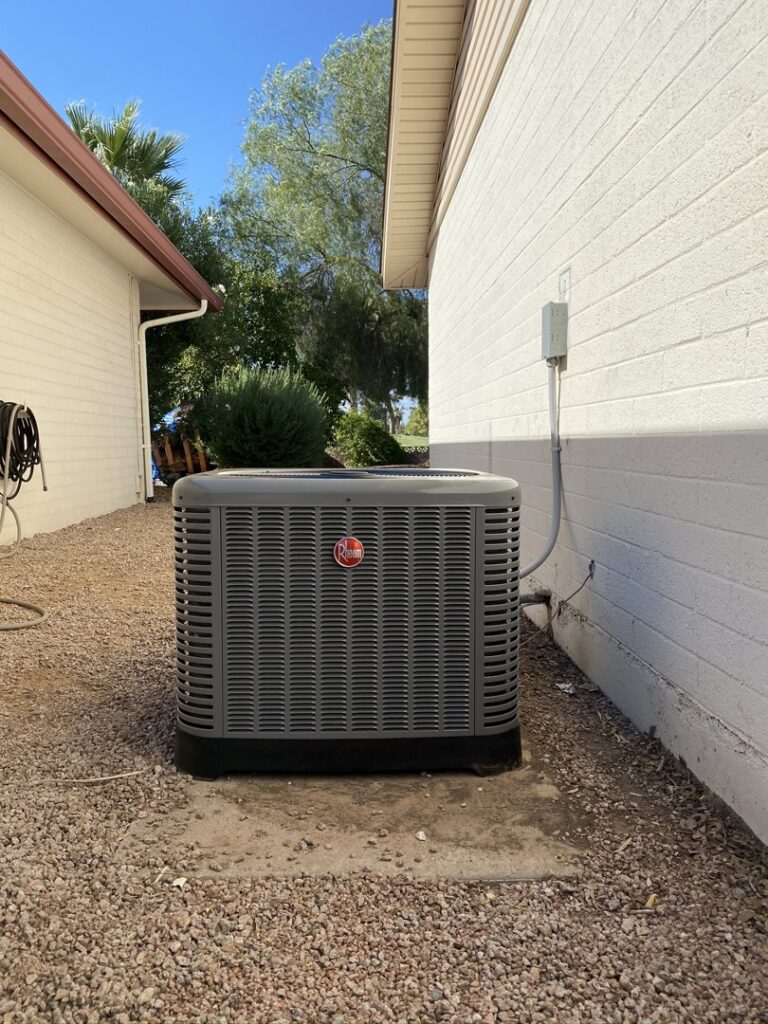 A Rheem AC condenser unit installed next to a white house by Kings of AC, LLC in Queen Creek, AZ.