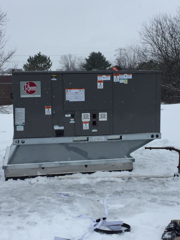 A large Rheem commercial HVAC unit sitting in the snow, ready for installation or service by Spencer Heating & Air Conditioning in Norcross, GA.