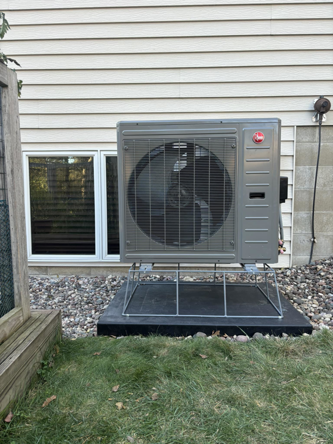 A newly installed Rheem heat pump outdoor unit next to a house by BRY Heat and Air in Elgin, MN