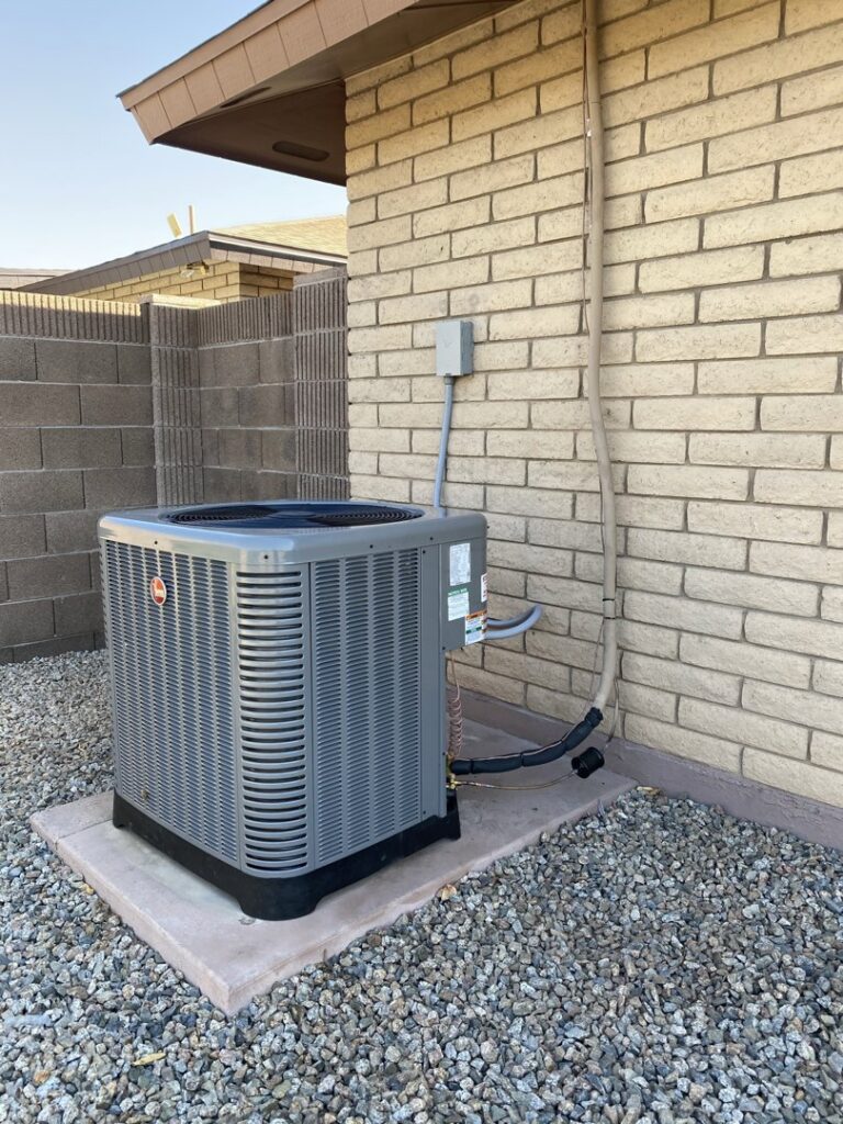 A Rheem outdoor AC unit installed next to a brick house by Kings of AC, LLC in Queen Creek, AZ.
