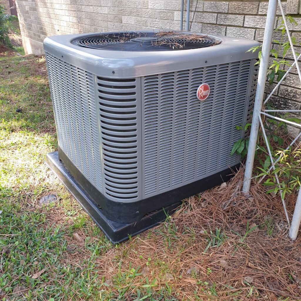 A Rheem outdoor HVAC condenser unit installed next to a residential brick house by Home Shield Heating and Air in Shreveport, LA.