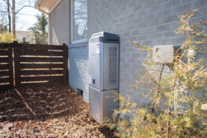 A Rinnai tankless water heater installed on a home with grey siding by Travis Crawford Heating, Cooling, Plumbing & Electrical in Charlotte, NC.