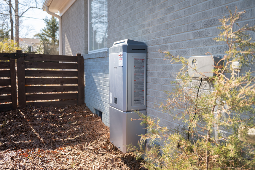 A Rinnai tankless water heater installed on a home with grey siding by Travis Crawford Heating, Cooling, Plumbing & Electrical in Charlotte, NC.