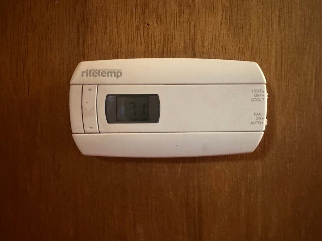 A RiteTemp thermostat installed on a wooden wall by Metro Air Conditioning, Heating & Services in Dallas, TX