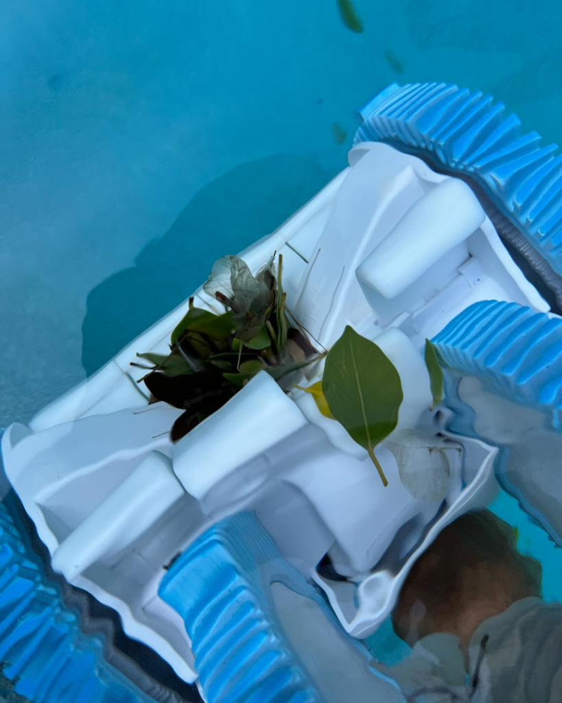 A robotic pool cleaner actively collecting leaves and debris from a swimming pool for The Pool Service Pros in New Hill, NC.