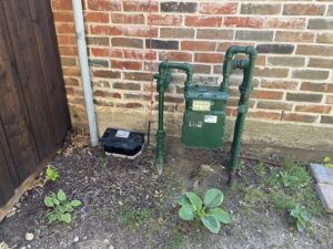 A rodent bait station placed near a gas meter against a brick wall by Drapers Pest Management in Fort Worth, TX.