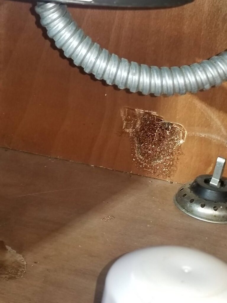 Steel wool packed into a hole in a wooden cabinet for rodent exclusion, a service by Corsello & Son Pest Control Services in Atlanta, GA.