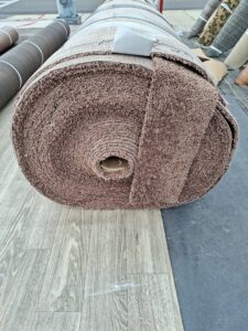 A large roll of brown textured carpet resting on other flooring materials, available at AFAB Carpets in Tampa, FL.