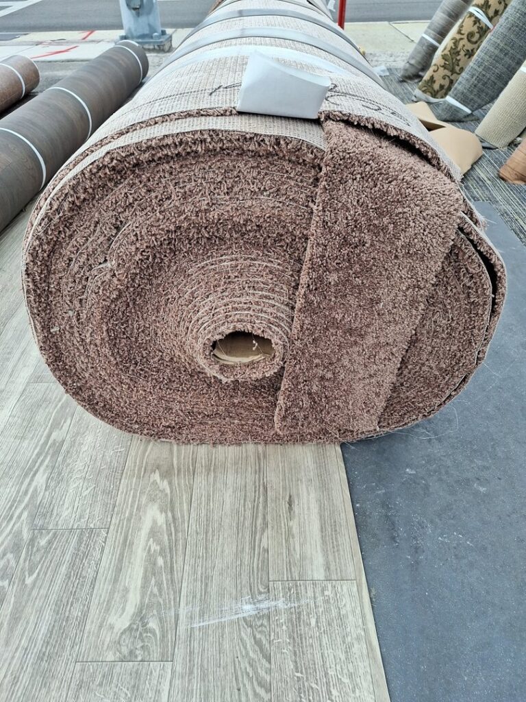 A large roll of brown textured carpet resting on other flooring materials, available at AFAB Carpets in Tampa, FL.