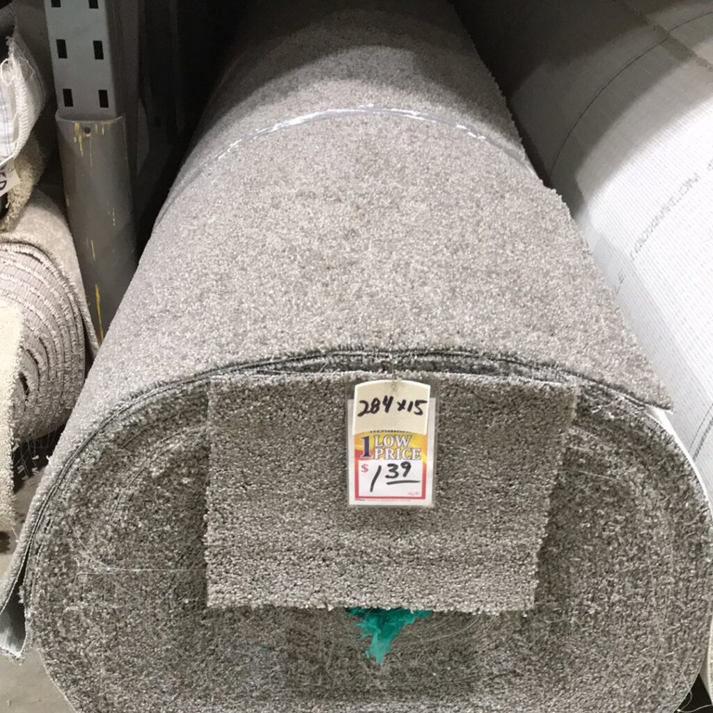 A large roll of grey textured carpet with a 'Low Price' tag, available at Gator Carpet and Tile in Jacksonville, FL.