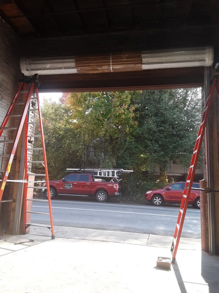 A new roll-up garage door being installed with ladders by Gilliam Services LLC in Johnson City, TN.