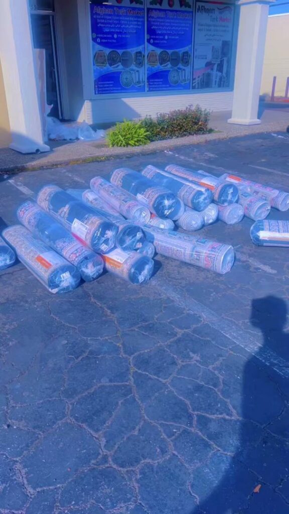 Several rolled carpets wrapped in plastic lying on the asphalt outside Afghan turk carpet online in Sacramento, CA, ready for delivery.