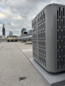 An outdoor air conditioning unit on a rooftop with the Chicago skyline in the background, serviced by Hvac Buddies in Chicago, IL
